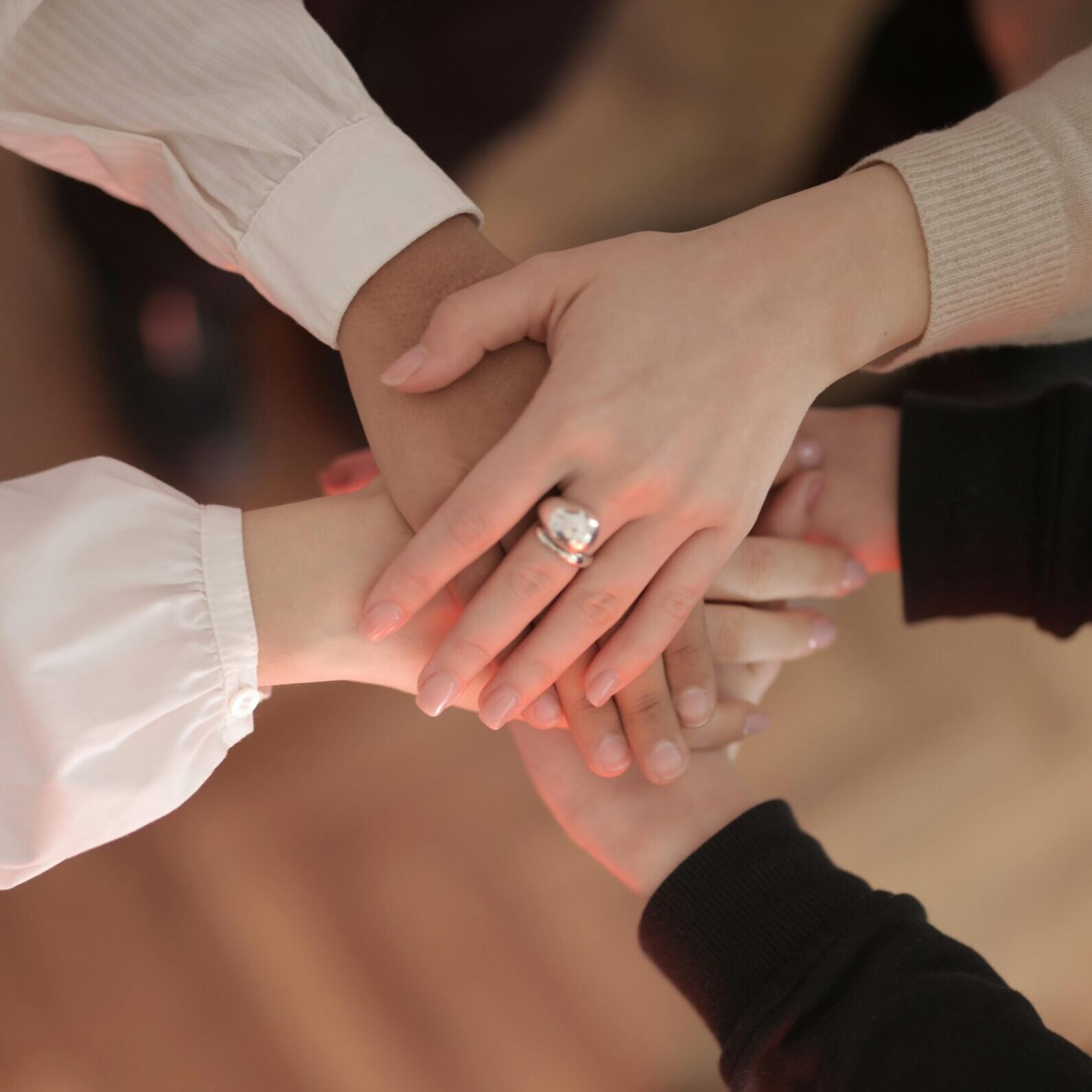 Top view of faceless friends in different clothes stacking hands together while standing on wooden floor indoor on sunny day